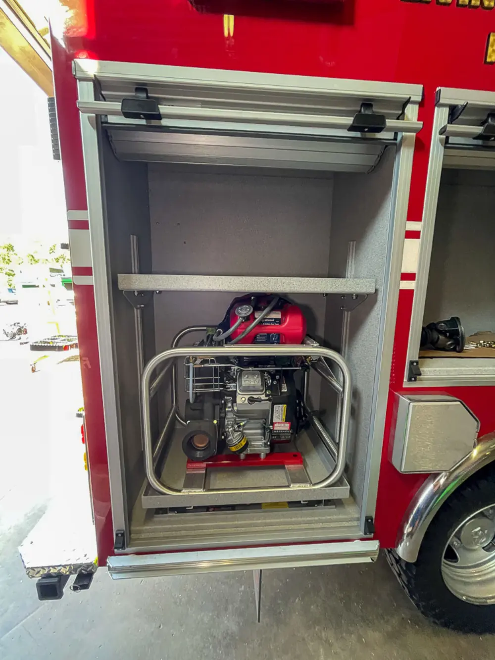 Exterior view of small fire truck showing cab, body compartments, and wheel/tire area.